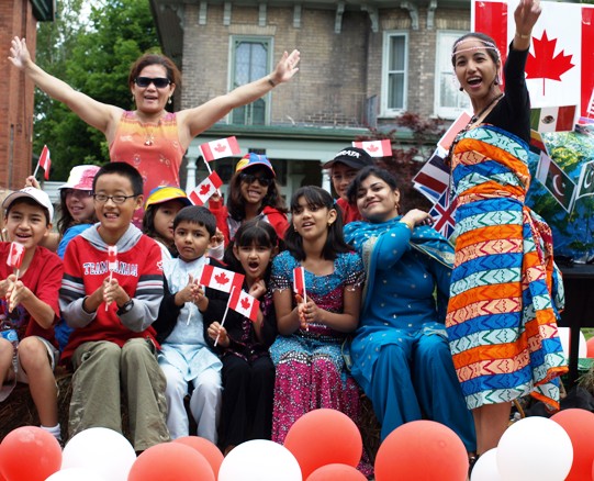 multicultural adults and children smiling and waving Canada flags as part of Canada Day celebrations