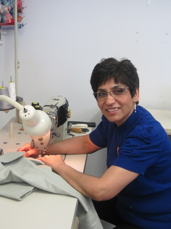 Farah Zafarzadeh smiling as she works at a sewing machine for her clothing repair and alteration business, First Stitch