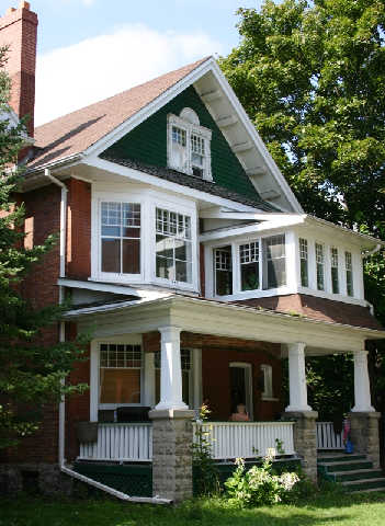 Outside view of the front of a Fleming Place home with a large covered porch and lots of windows, surrounded by tall trees