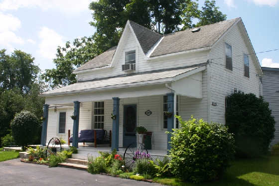 Older white house on Parkhill Road in Peterborough with covered front porch, blue trim, and a beautiful garden