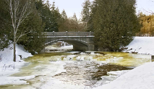 Concrete arch bridge over Jackson Creek in Jackson Park with snow-covered banks and ice in the water