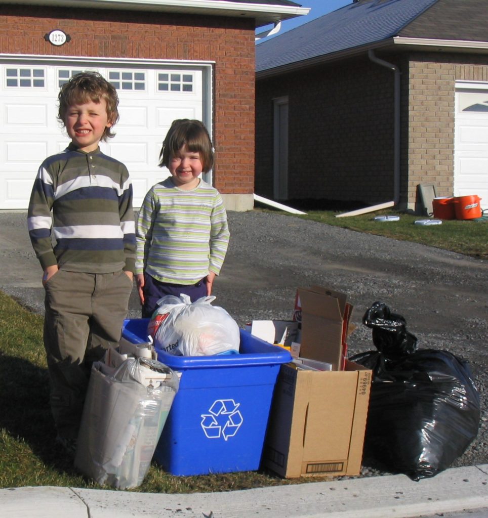 Young boy and girl standing behind garbage and recycling on the curbside that's ready to be picked up
