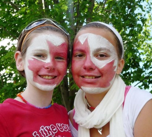 2 smiling children with faces painted white with large red maple leaves for Canada Day