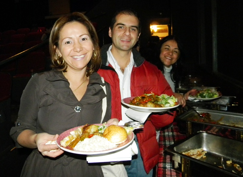 Three young adults holding plates full of food and smiling at a multicultural event